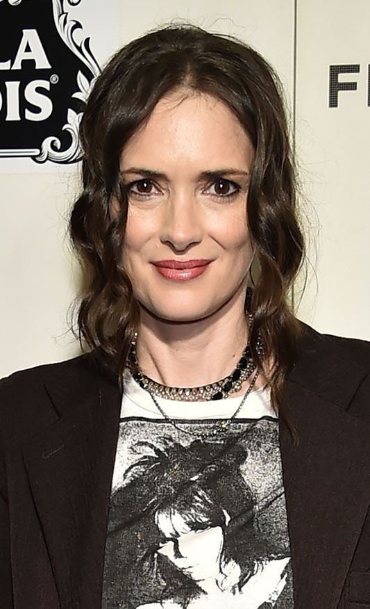 older winona ryder, bust image, wearing a t shirt and a blazer with necklaces