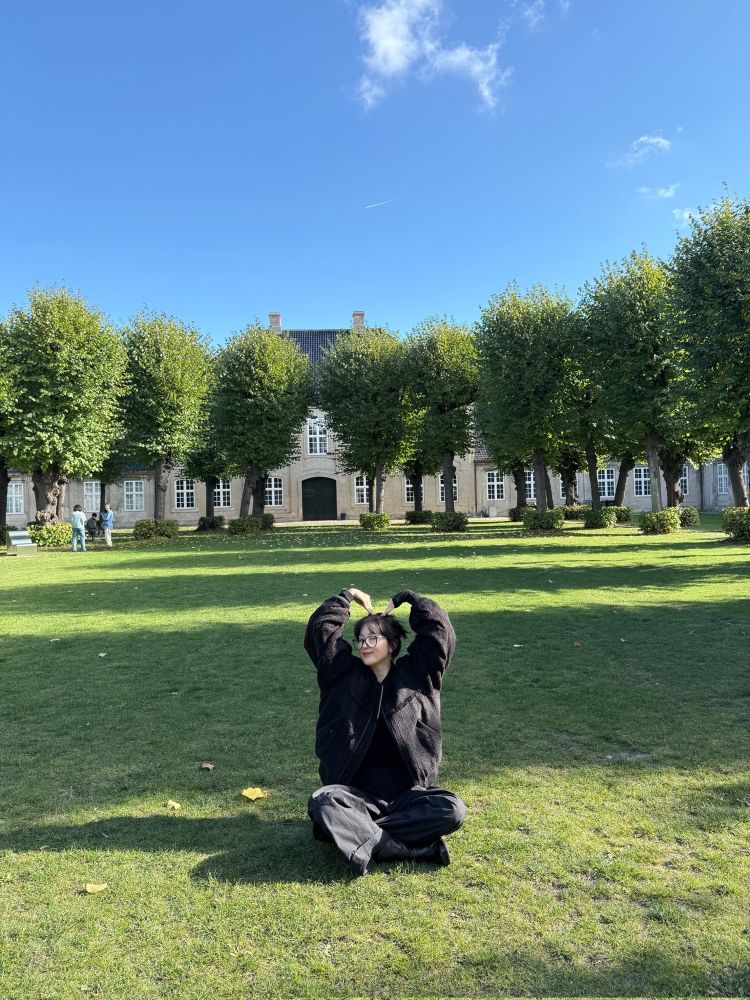 red velvet’s seulgi sitting in a park in copenhagen, making a heart shape with her arms over her head