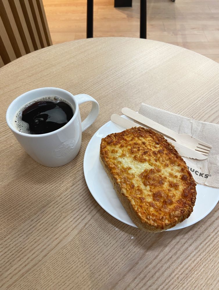 On a table in a Starbucks in Slough, a mug of coffee and a (weirdly chewy) cheese toastie on a white plate.