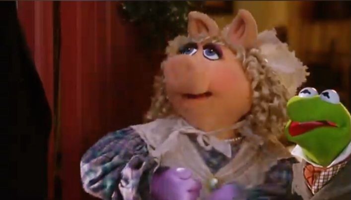 A scene from The Muppets Chtistmas Carol in which Miss Piggy, dressed in Victorian clothes & cap, is playing Mrs. Crachit. She's raising her purple gloved hands about to hit Mr. Scrooge, played by Michael Caine. Kermit the Frog as Bob Crachit is horrified & tries to intervene. TMCC is the best! 