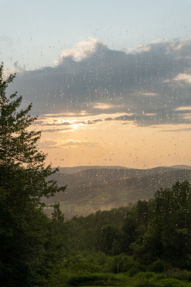 Photo through a rainy window of a sunset over green mountains.