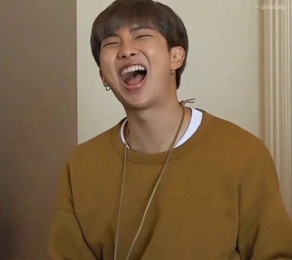 a man wearing a yellow sweater is laughing with his mouth wide open