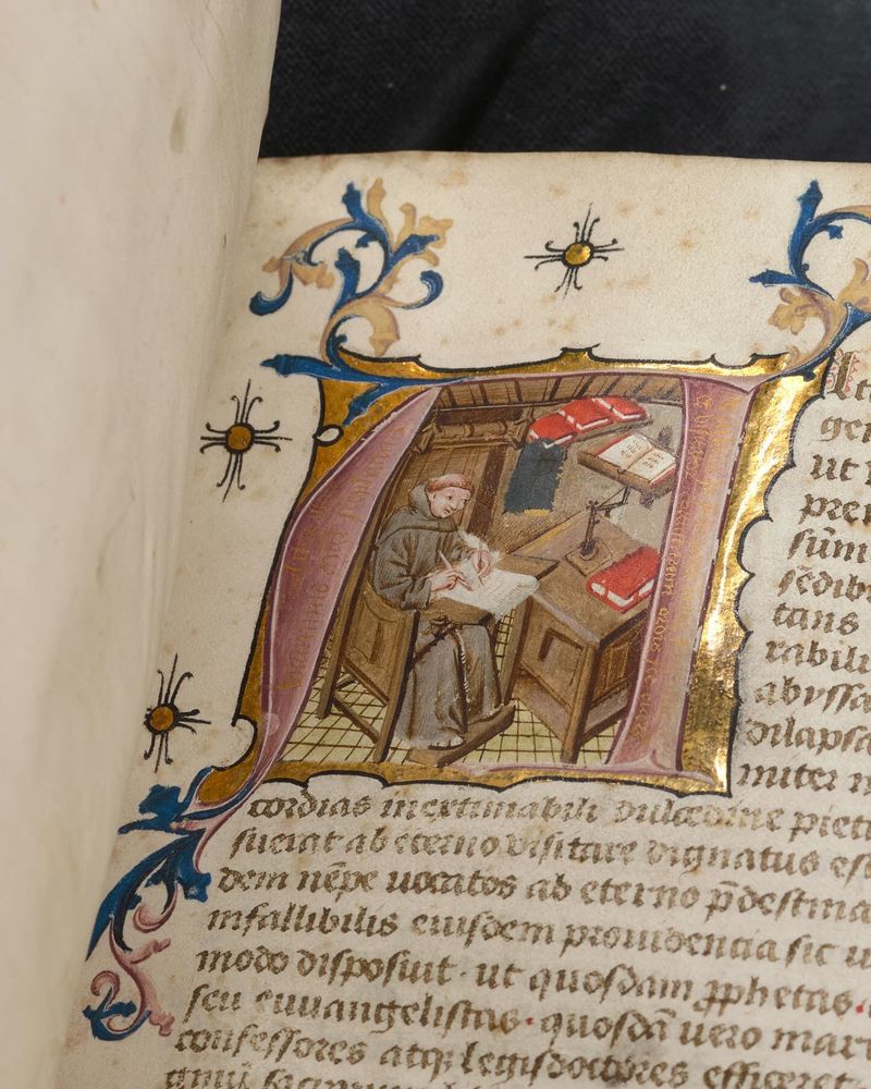 Een rijk versierd initiaal in een middeleeuws handschrift. Getoond wordt een schrijvende monnik, Stephanus de Juliaco. De rand van de afbeelding is met goud bekleed.