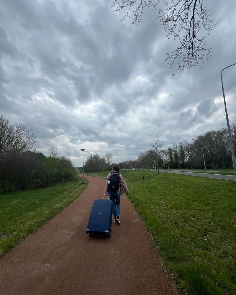 Een vrouw loopt met een grote rolkoffer over een voetpad.