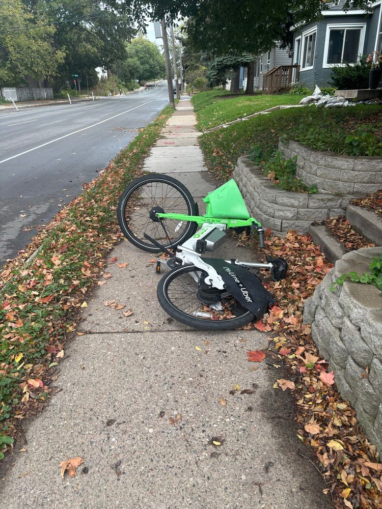 A lime bike square in the middle of a sidewalk, entirely blocking the way a person walking or rolling needs