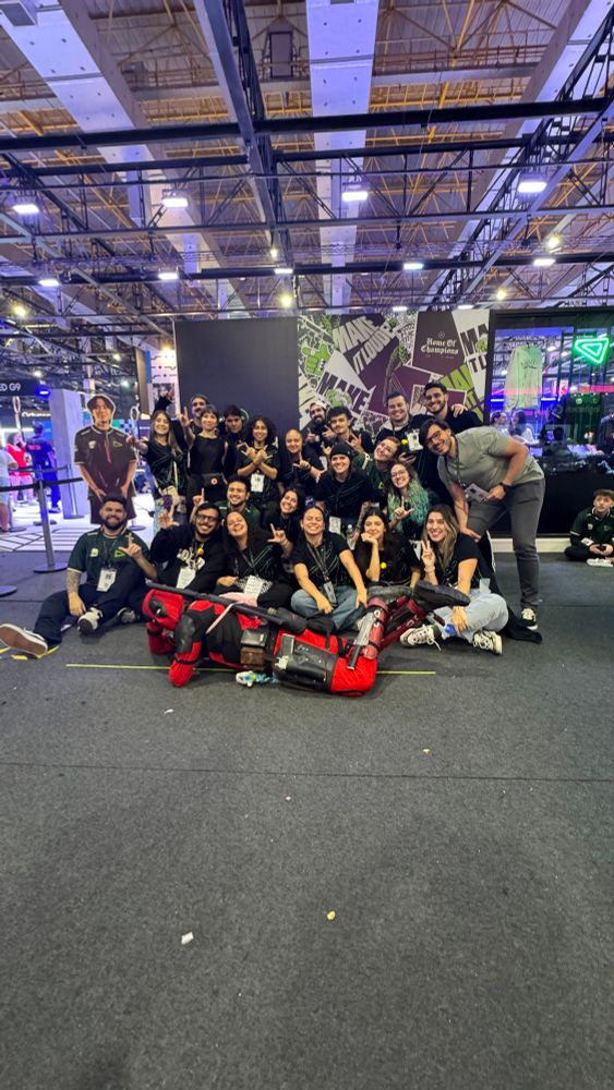Foto de boa parte da staff da LOUD que trabalhou na BGS posando em frente ao stand. Algumas pessoas estão abaixadas, outras de pé, algumas fazendo o L com a mão e também há um boneco de papelão do Croc.
