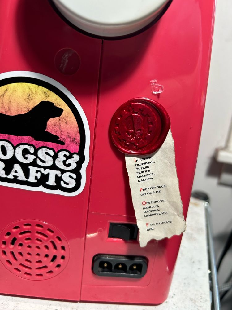 A red sewing machine decorated with a purity seal with the sigil of the Adeptus Mechanicus and a series of Latin supplications to the Machine Spirit.