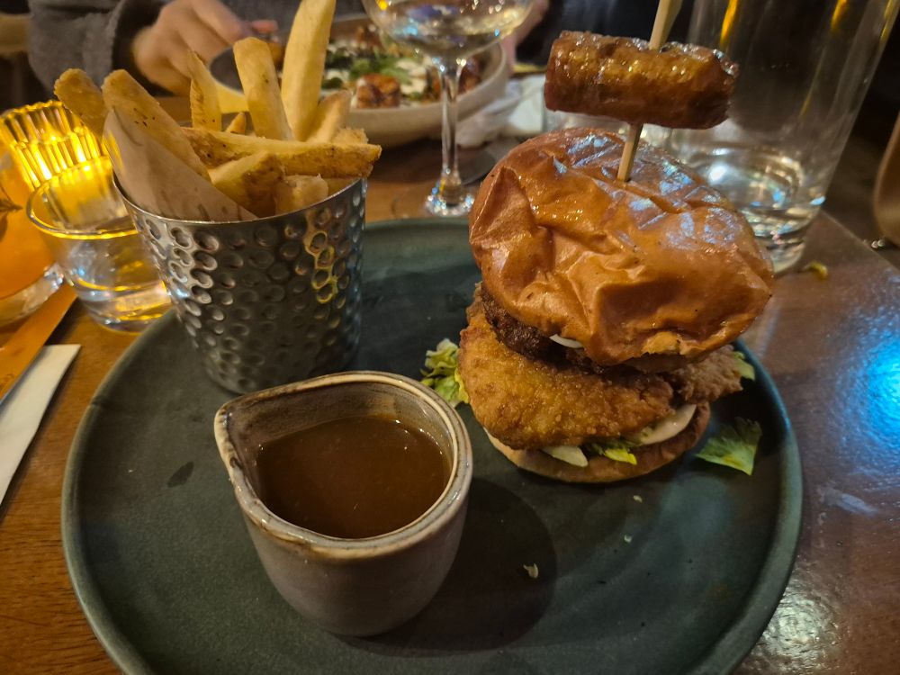 A burger with chips, gravy, and a sausage speared on top.