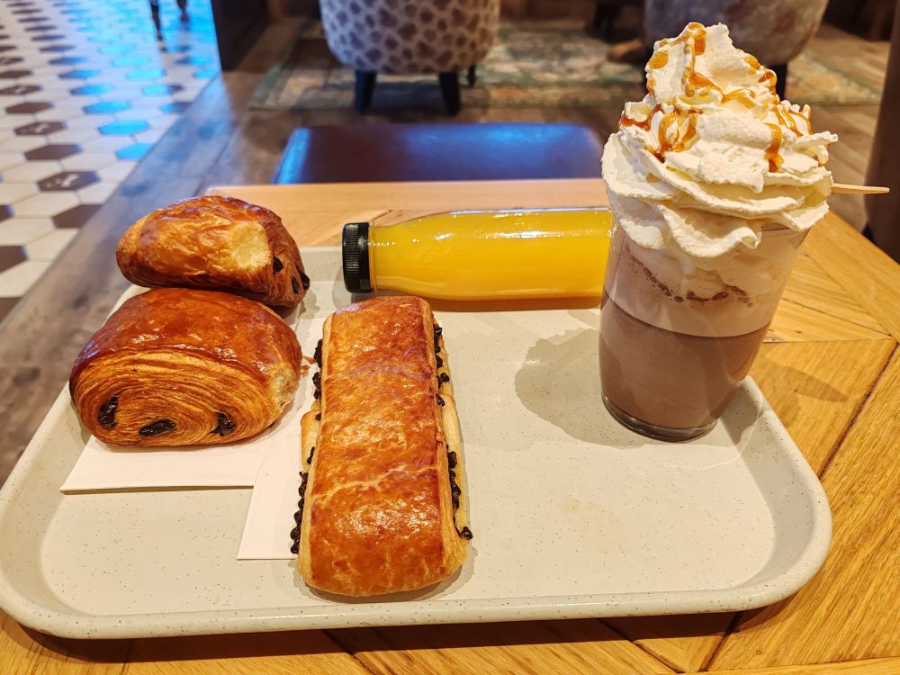 Plateau avec deux pains au chocolat un pain suisse une bouteille de jus d'orange et un verre de chocolat Viennois 