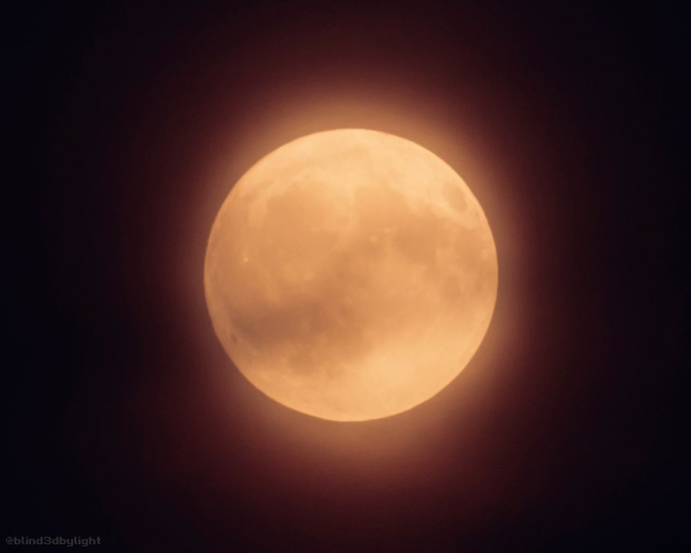 Photo of the full moon, tinted red and somewhat softened by haze.
