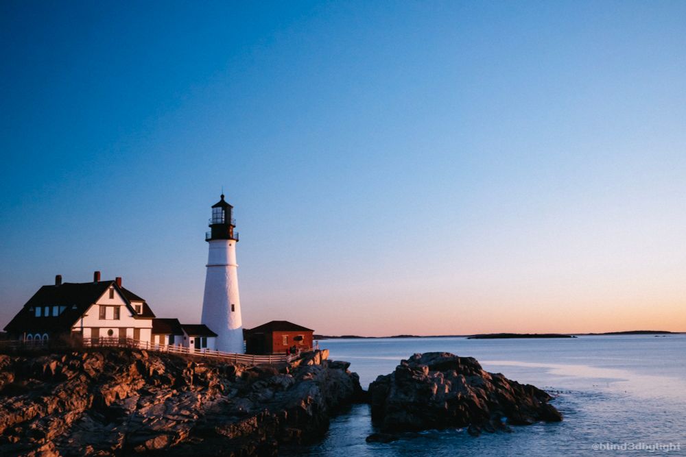Photo of the Portland Head Light at sunrise, taken from a distance.