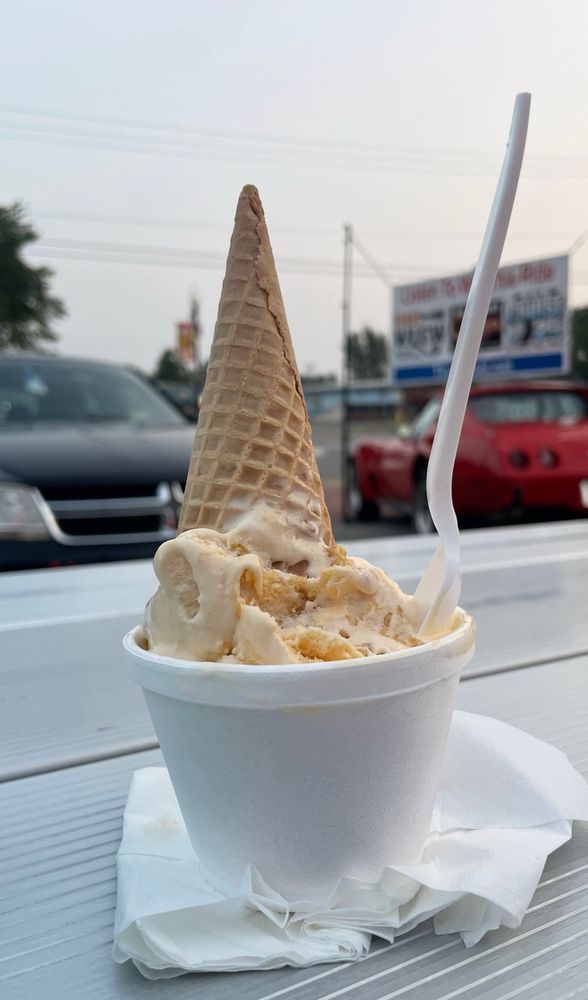 A picture of a banana ice cream cup on a metal picnic table with cone and spoon sticking out of it