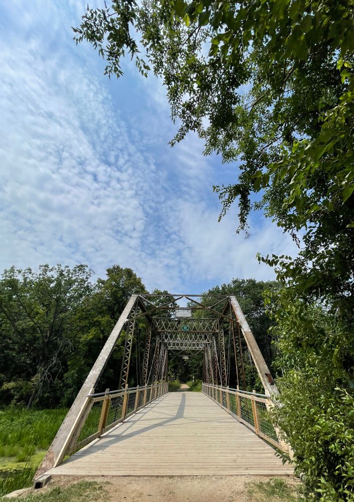 Steel bridge going over a marsh heading to a trail with a cloudy sky