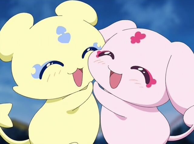 Mepple and Mipple from the 2004 anime Futari Wa Pretty Cure. Mepple (left) is a small, round, yellow creature with bearlike ears and blue markings on his face. Mipple (right) is the same size and pink, with a chubby rounded face, floppy rabbit-like ears and dark pink markings on her face. The pair are hugging each other and smiling
