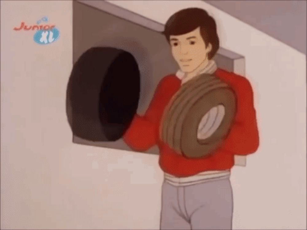 a man in a red sweater is holding a tire in his hands in front of a wall .