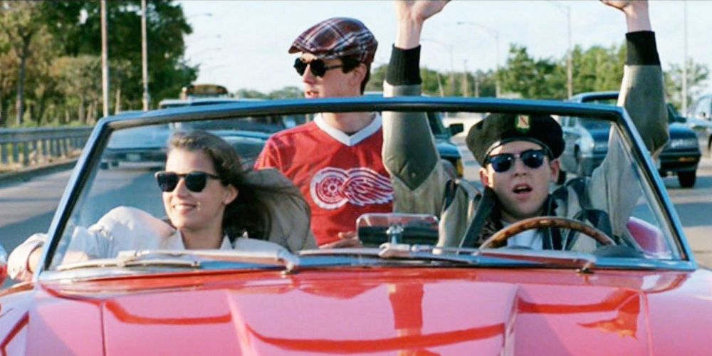 Three principal actors from Ferris Bueller’s Day Off in red sports car. Matthew Broderick is driving but his hands are not on the wheel. 