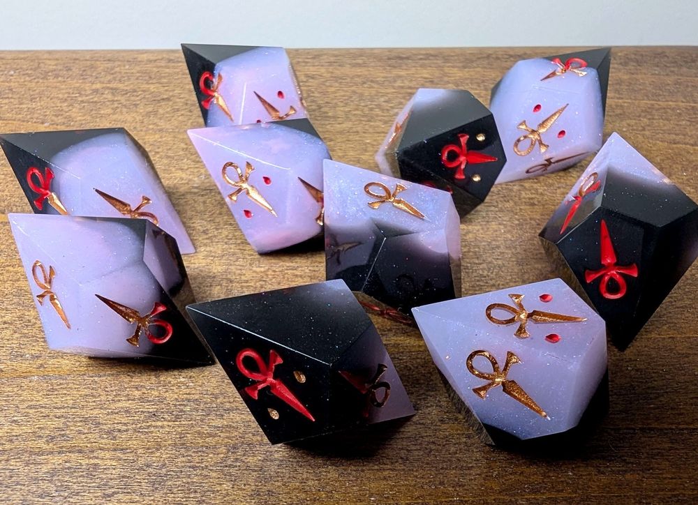 ten sided dice for vampire the masquerade. These sharp edged dice are half black, half shimmery pastel purple. On the black sides they are inked in red, and on the pastel purple sides they are inked in copper. They show ankh symbols instead of numbers. 