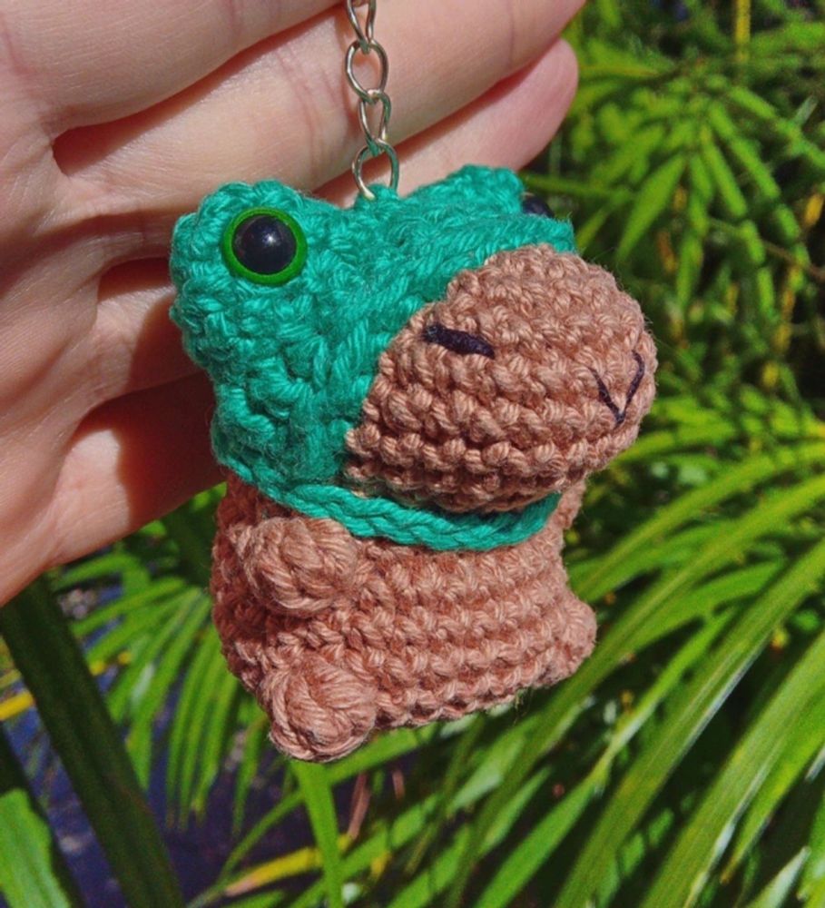 um chaveiro de capivara com touca de sapinho de amigurumi (crochê) feito por @polvigurumis.bsky.social