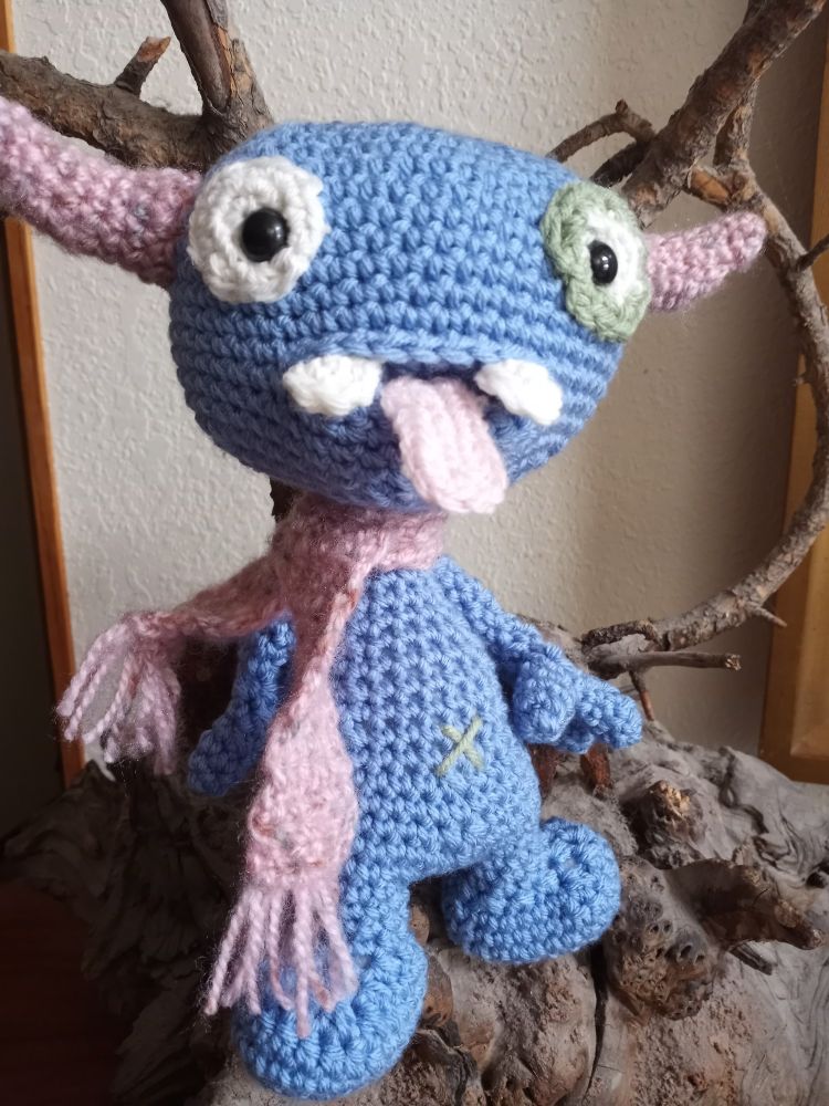 Blue amigurumi monster with horns and a sticking out tongue