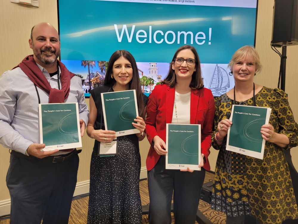 4 people stand holding a green report titled Public's Case for Curators in front of a screen that reads Welcome! 