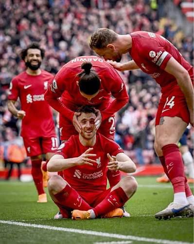 Diogo Jota of Liverpool FC celebrates a goal by sitting cross legged on the field while a teammate embraces him