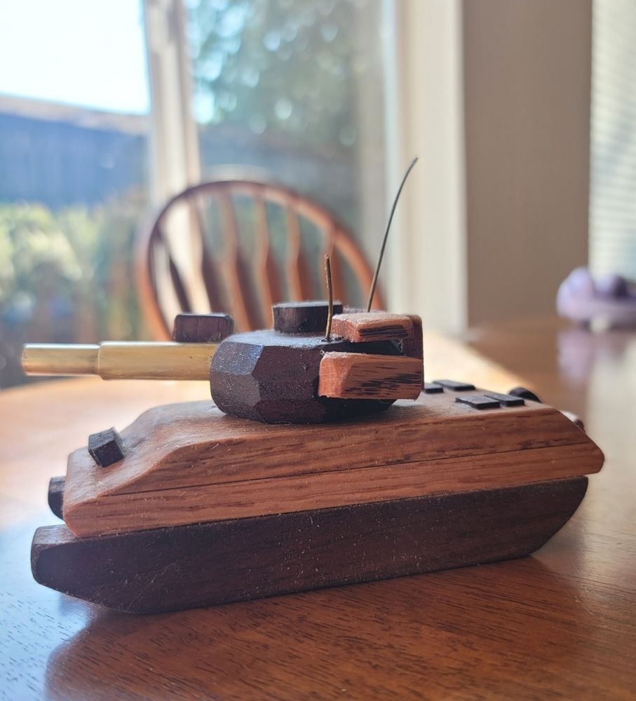 A small wooden tank sits on a brown kitchen table. Sunlight shines thru a big window in the background. 