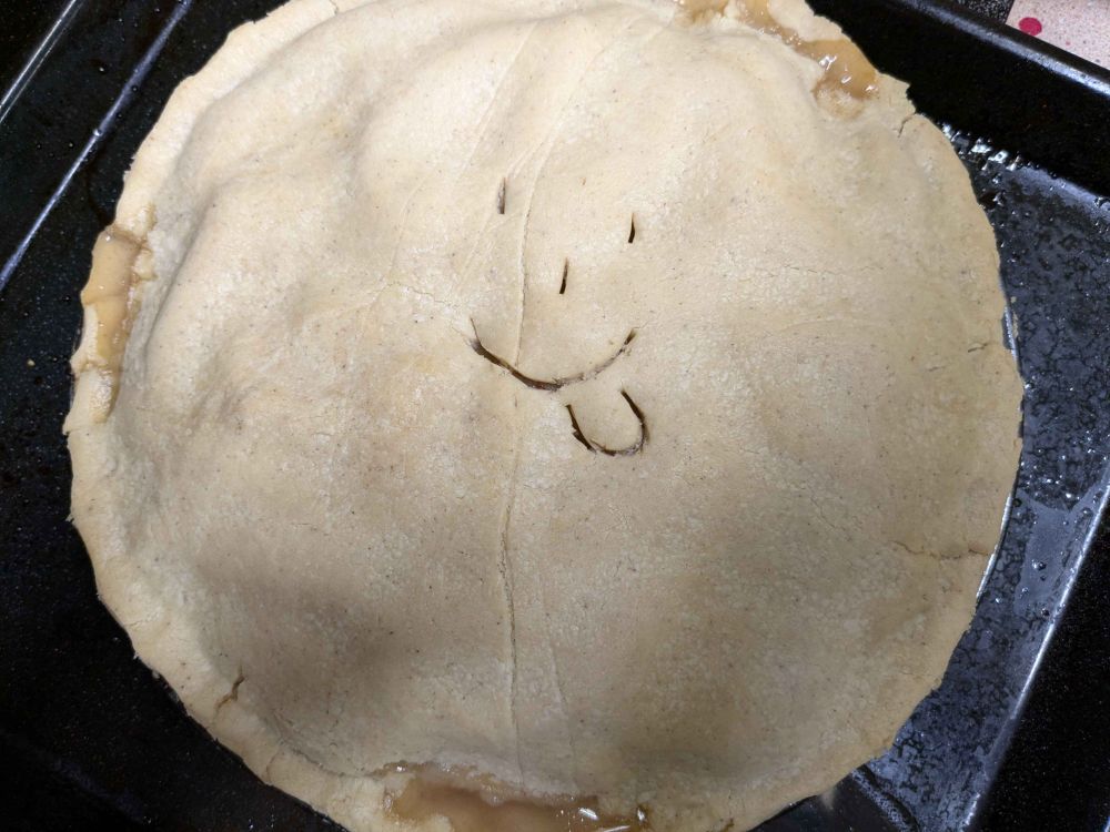 A double crust apple pie, hot from the oven, with the yum emoji cut into the top crust for venting purposes.