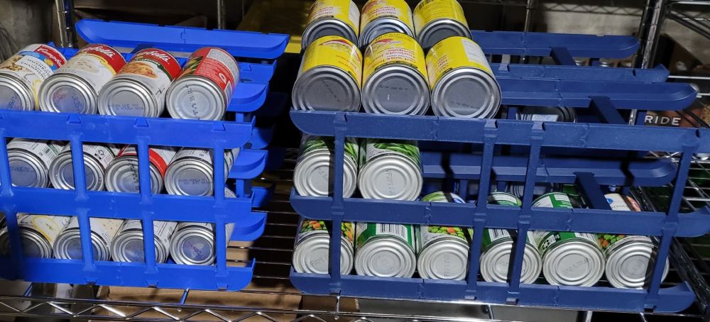 Soup and vegetable cans laying on blue 3d printed rollers, 3 rows high connected together and set at an angle for rolling to the front.