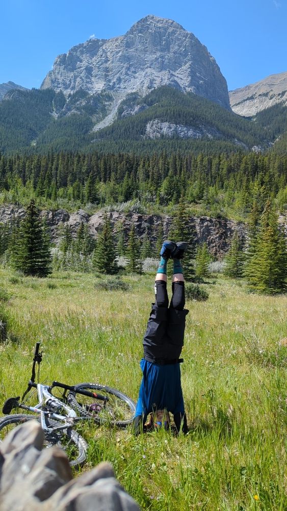Doing a headstand while on a break from a mountain bike ride with mountains in the background 