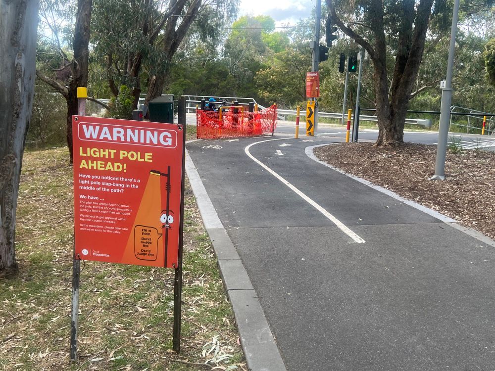 Warning sign “light pole ahead” with additional text saying they are working to fix it.