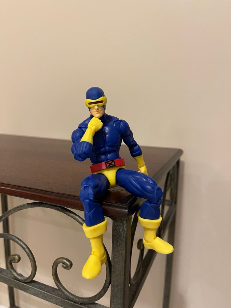 X-Men 97 action figure of Cyclops in his classic outfit. He is seated, leaning forward, and resting his chin on his right fist.