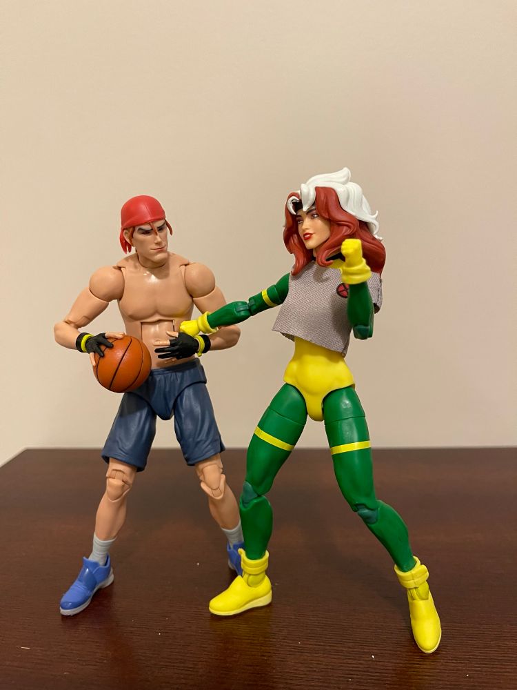 Gambit and Rogue X-Men 97 action figures in their basketball outfits. Rogue is punching Gambit in the gut and he keels forward as he clutches his stomach. 