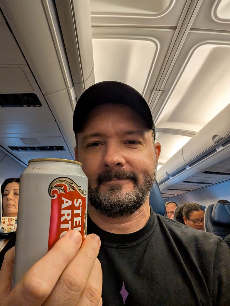 li'l ol' me on a plane to Stockholm, holding up an in-flight Stella Artois.