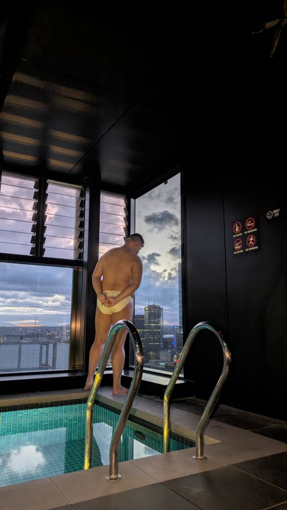 BudgyCub standing by the windows waiting for the sun to rise wearing a Teamm8 speedo