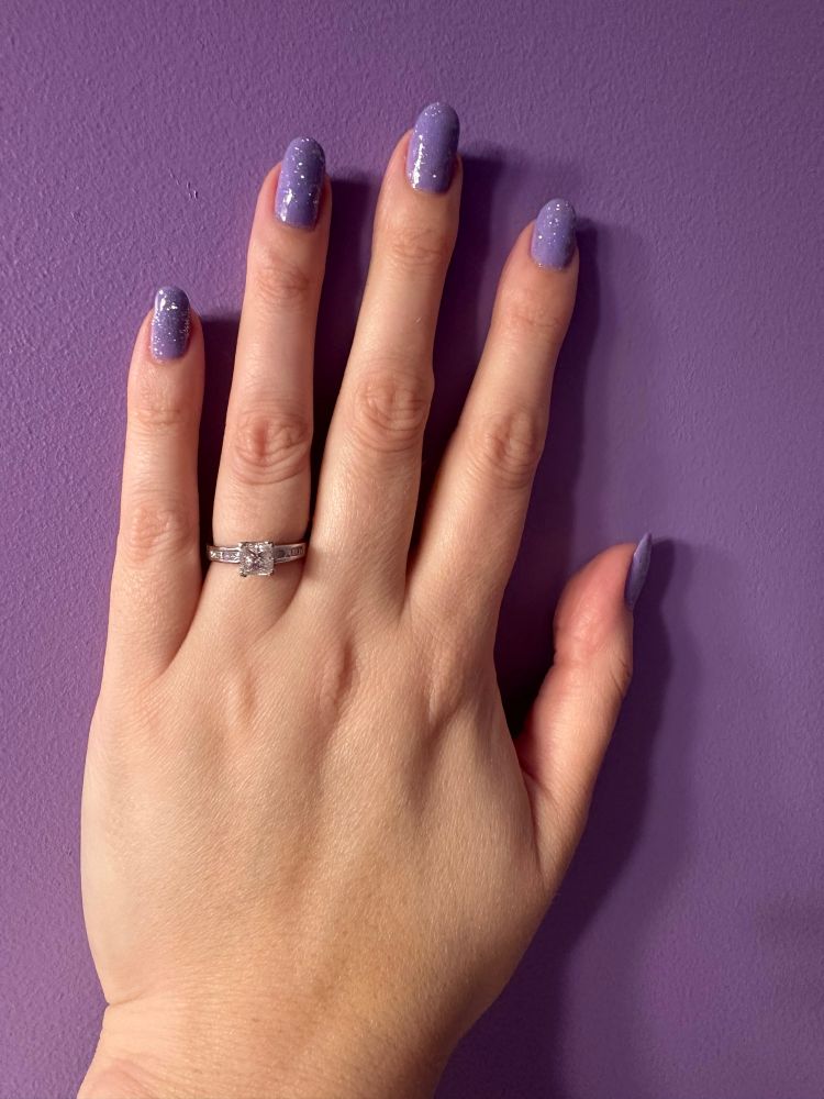 Amy's left hand on a purple wall, she has a sparkly purple manicure, and is also wearing her engagement ring. 