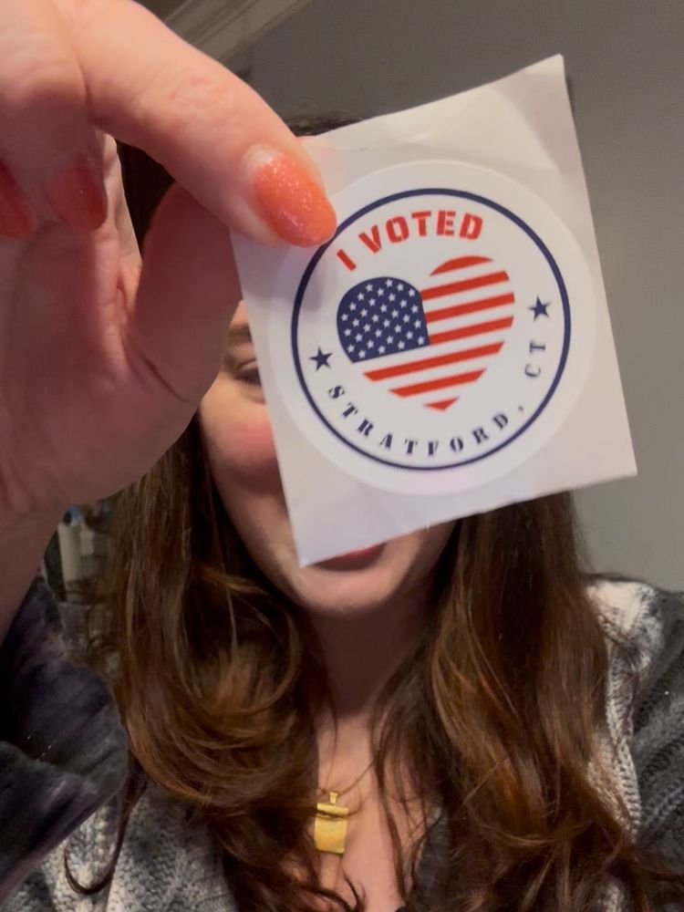 Amy holding up an "I Voted/Stratford CT" sticker to the camera, obscuring her face 