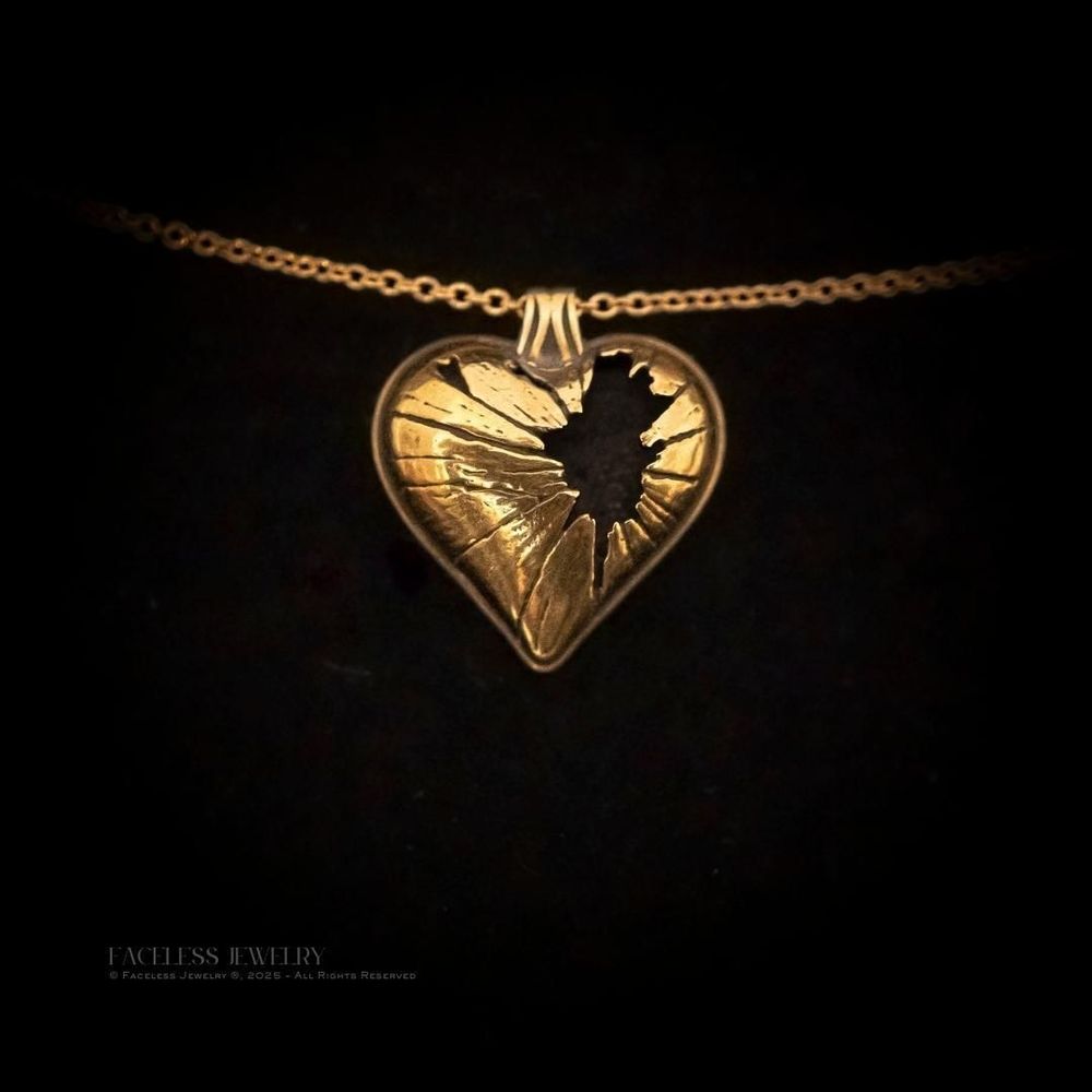 18kt Golden Shatter pendant lying against a black background, the fractured heart design catching subtle highlights.