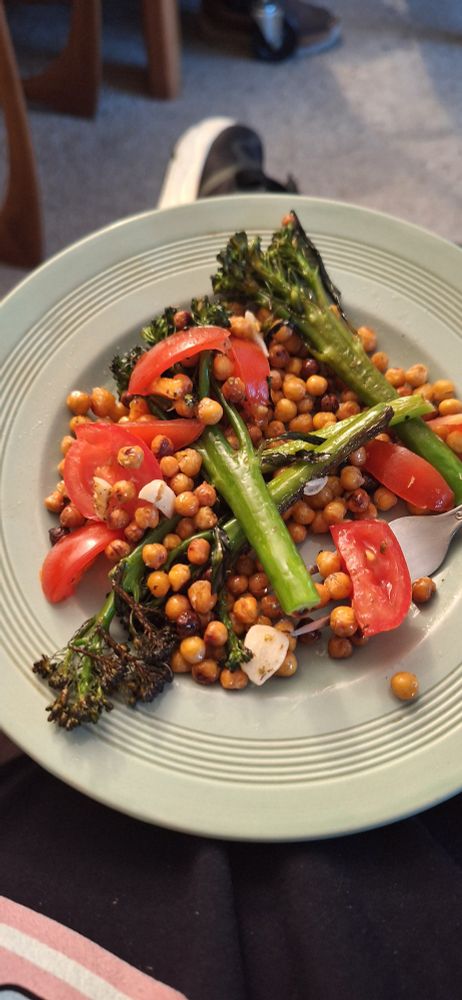 A turquoise plate with golden chickpeas, bright red chunks of fresh tomato and long green tenderstem broccoli with charred edges