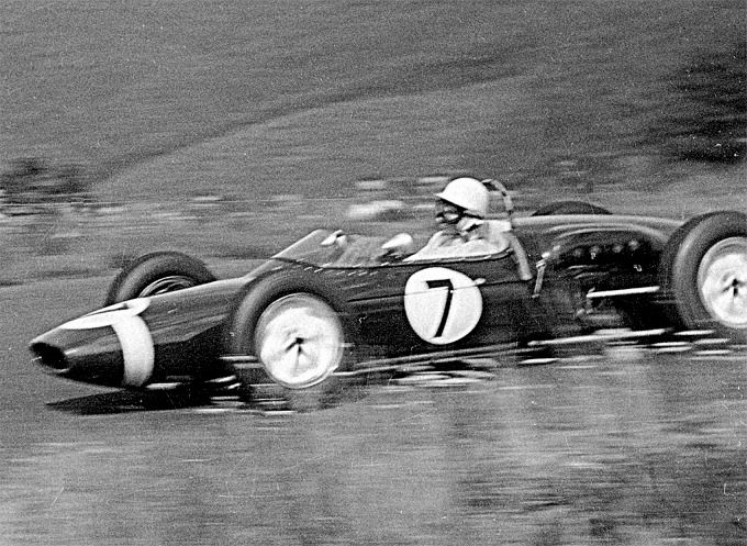 A black and white photo of a Lotus 21 in front of tall grass.