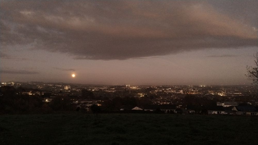Moon at dusk over city lights in the distance