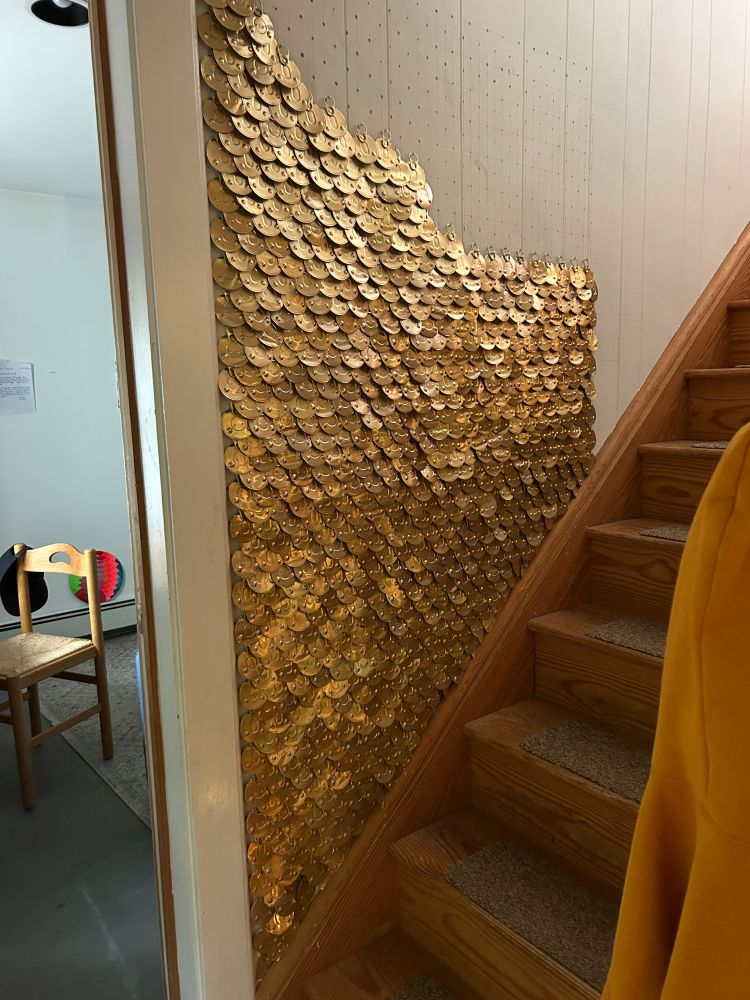 a photo of a wall adjacent a staircase that has been sequined with gold cat food can lids
the penciled grid is visible on the bare part of the wall