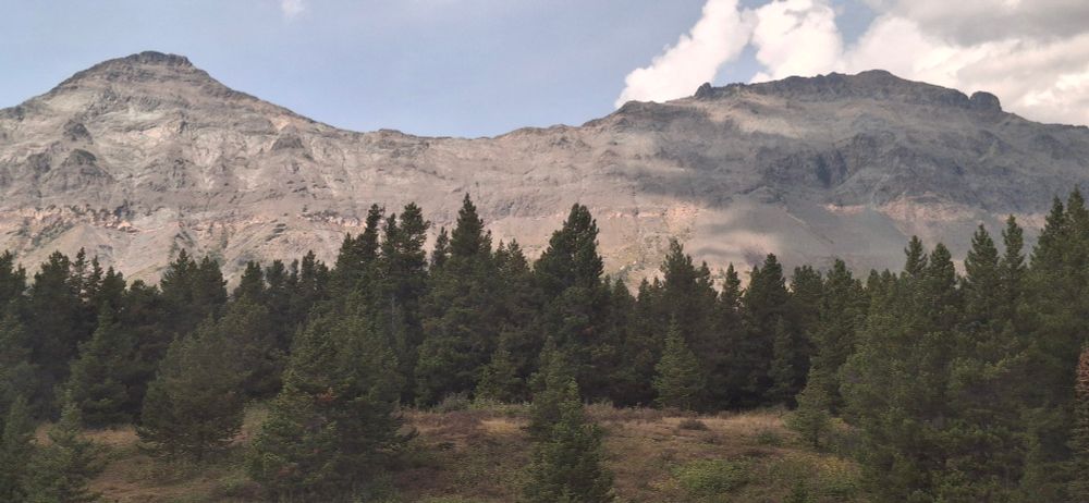 Two rocky mountain peaks, one in shadow and one in sunlight, stand above forest and meadowland in Montana
