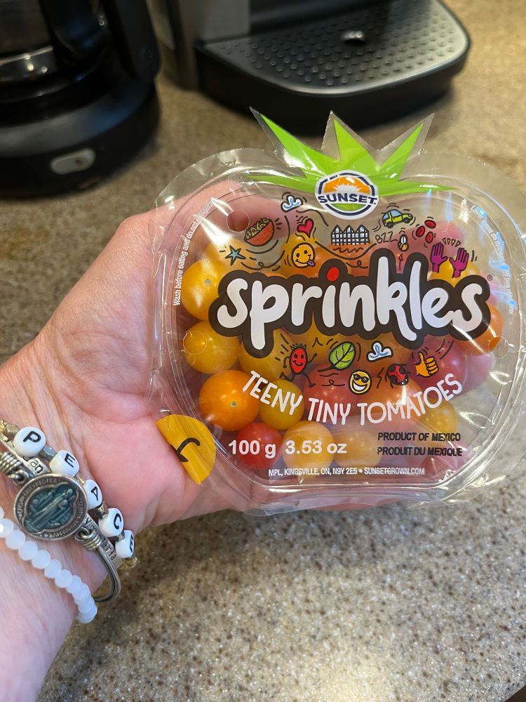 In my hand there’s a little tomato-shaped container of tiny red, yellow, and orange “Sprinkles” tomatoes. 