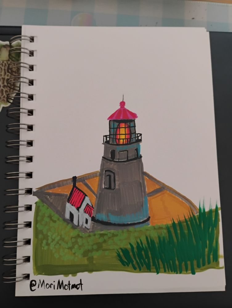 Grey lighthouse with a white house on its left with a red roof. In the foreground is some greenery and grass.