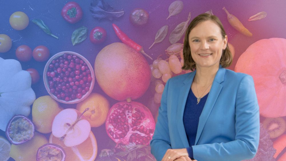 An image of Dr. Annalijn Conklin, from the torso up, wearing a blue outfit. Her photograph is superimposed over a picture of fresh produce, including apples, lemons, and grapes, that is tinted purple. 