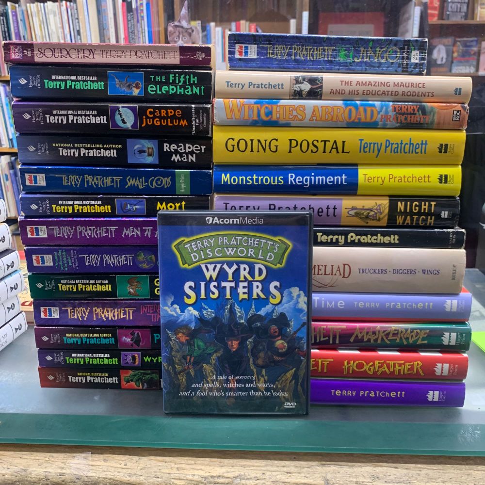 A DVD of the TV animated movie Wyrd Sisters, based on the book by Terry Pratchett, is posed against two stacks of Terry Pratchett books.