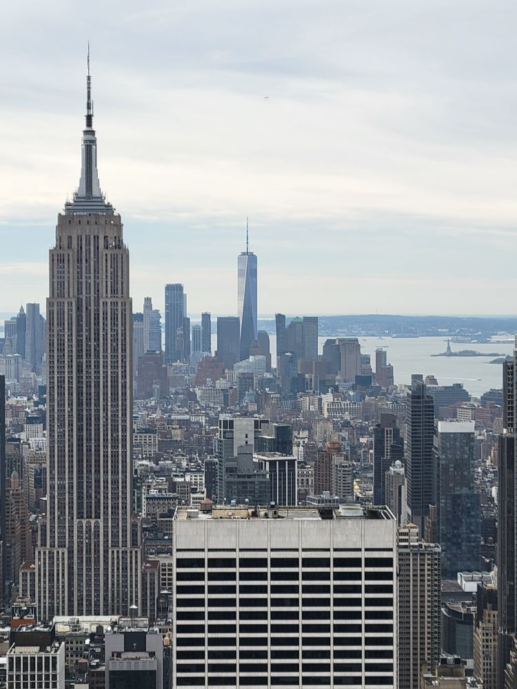 A view from Top of the Rock of the NYC cityscape, with the Empire State Building in view, as well as a tiny Statue of Liberty.