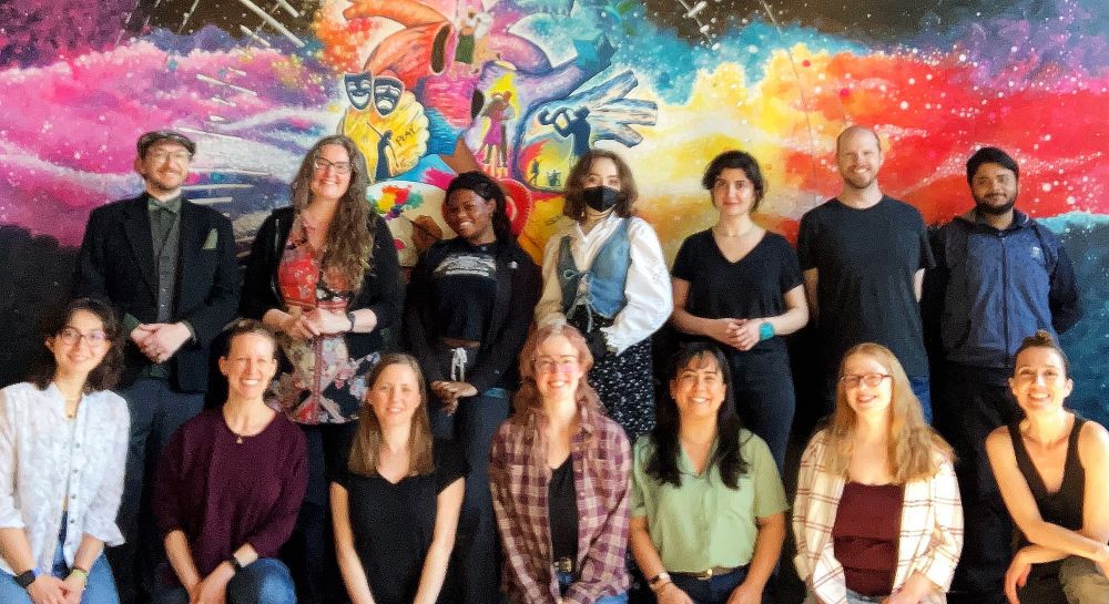 A large group of artists pose for a group photo in front of a mural.