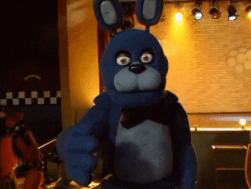 a blue stuffed animal is pointing at the camera in a dark room