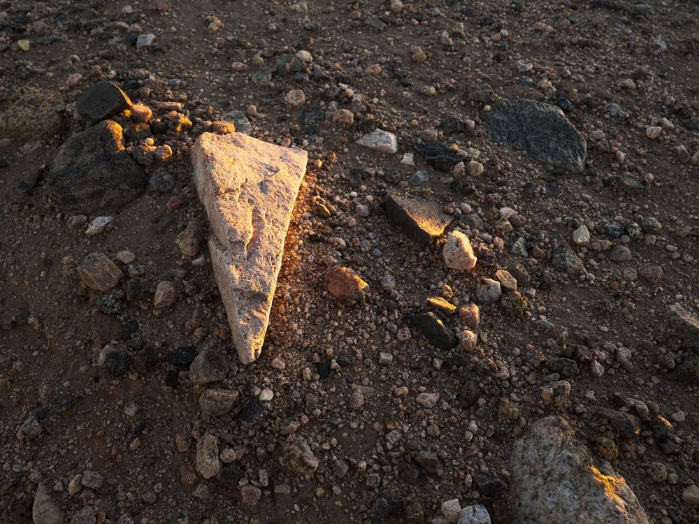 Triangular rock lit by skimming sunrise light amid pebbles and sand.